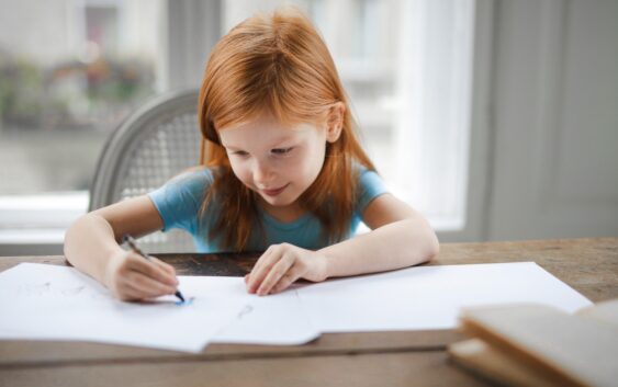 Diligent small girl drawing on paper in light living room at home